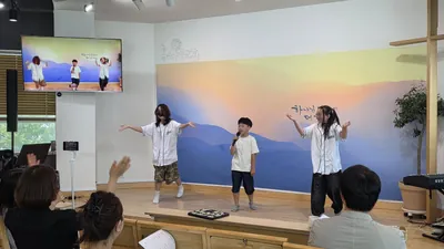 예배당 무대에서 팔을 벌리고 춤추는 아이들과 앉아서 지켜보는 사람들