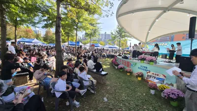 무대 위 공연자와 나무 그늘 아래 앉은 수백 명의 축제 관객