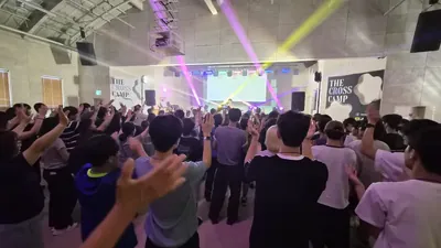 색색의 조명 아래 손을 들고 노래하는 사람들의 뒷모습