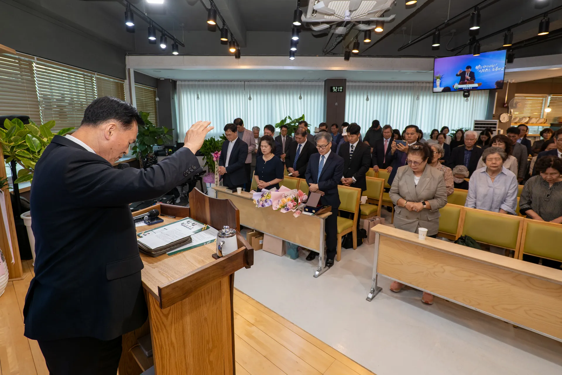 예배 공간에서 손을 들고 축복하는 목사와 자리에 선 교인들