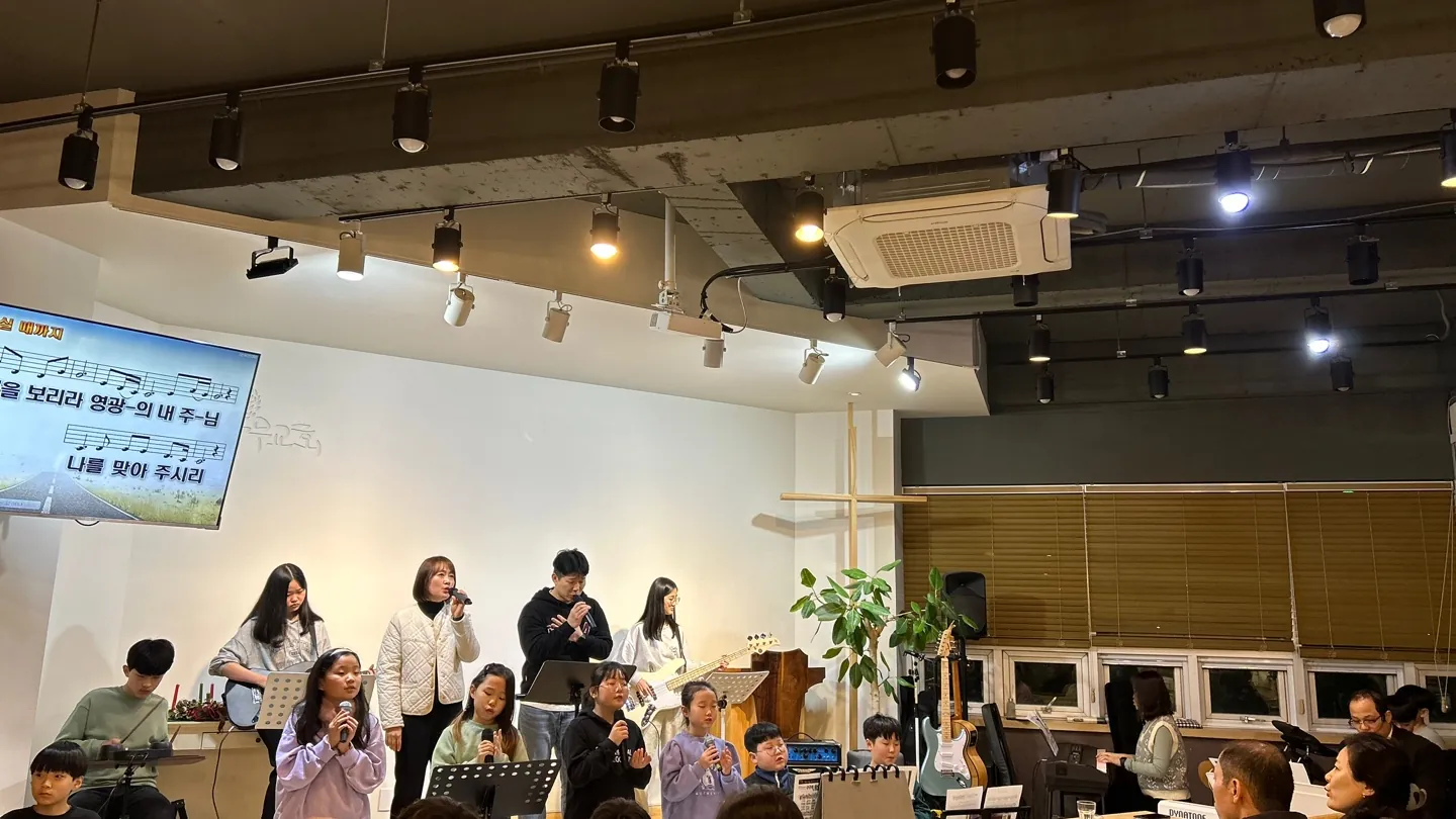 성탄 장식 옆 무대에서 악기와 함께 노래하는 사람들과 자리에 앉은 교인들