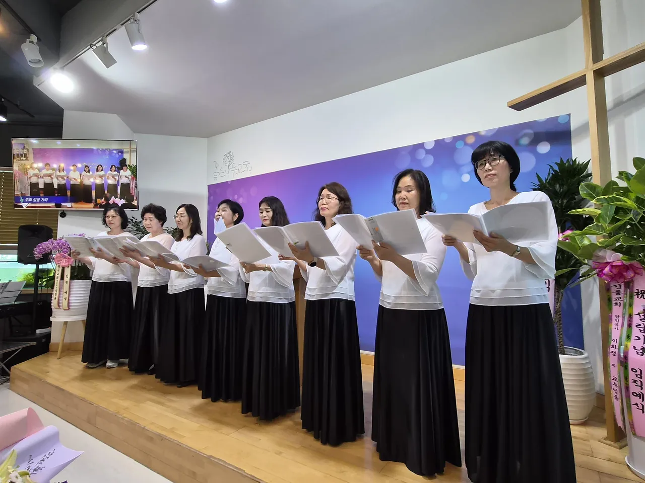 무대 앞에 나란히 서서 악보를 들고 함께 노래하는 사람들